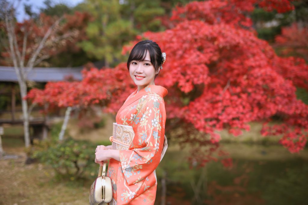 京都の紅葉を背景にオレンジ色の着物を着た女性のロケーション撮影